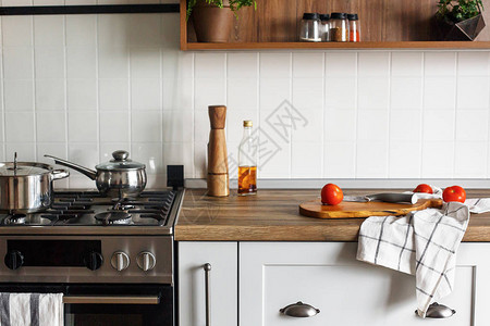 现代厨房台面上带刀西红柿橄榄油的木板和带平底锅的钢炉煮食物斯堪的纳维亚风格的时尚灰色图片