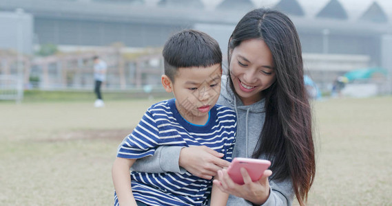 母亲和儿子在市公园与手机聊天图片