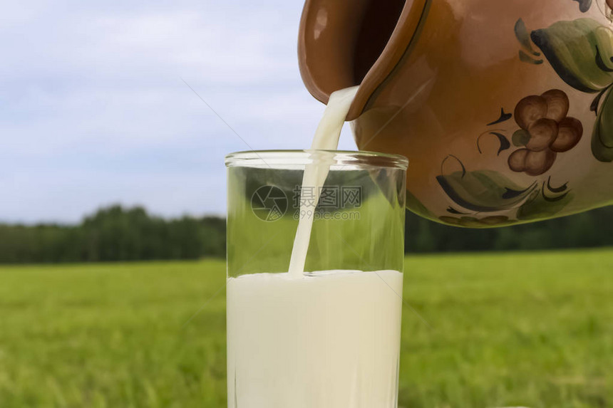 新鲜的天然鲜奶从陶瓷手工制罐子倒入玻璃杯瓶中图片