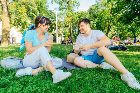 坐在绿草上吃汉堡喝冰沙的夫妇宽天使背景图片