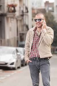 穿着时髦衣服的微笑男人在街上行走时用智能手机说话图片
