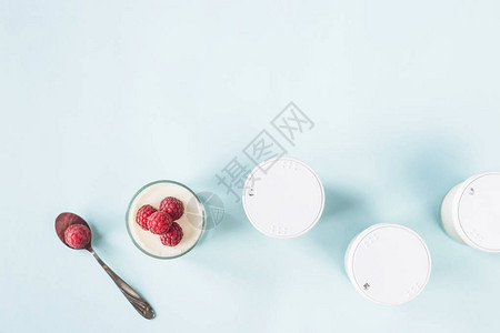 在蓝色背景的封闭罐子旁边有自制酸奶和草莓的开瓶罐图片