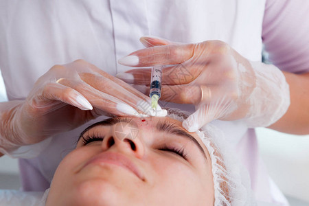 医生美容师在美容院里为一位美丽的年轻女子的面部皮肤进行了面部注射程序图片