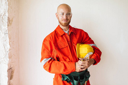 身着橙色工作服和防护眼镜的年轻工头手持黄色安全帽和工具图片