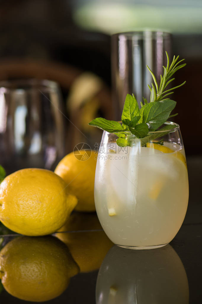 用迷迭香枝和薄荷叶装饰的柠檬水饮料玻璃杯柠檬躺在玻璃杯周围图片