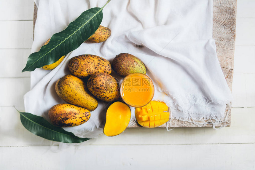 自然芒果和芒果汁在一张木桌上和一块白布上图片