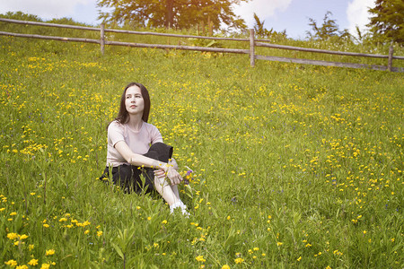 体贴的年轻女子坐在花草甸上夏日阳光明媚的日子图片