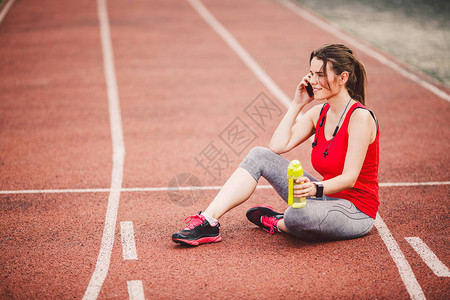 马尾辫在体育场的红色跑步赛道上锻炼后坐着休息图片
