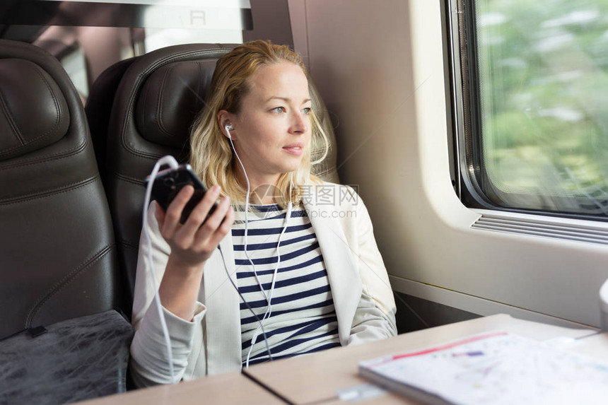 商业女商人乘火车乘坐公务舱座椅时使用耳机用手机进行电话交流请访问InfoFinland上图片