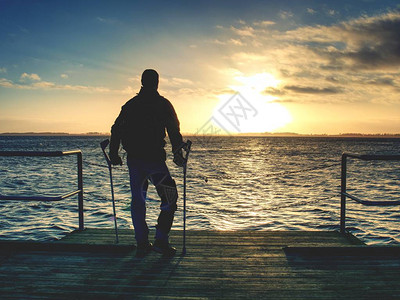 残疾受伤的徒步旅行者正在庆祝他的目标的单独依恋游客在温暖的日落天空接触海水的地平线上站在海桥上或背景图片