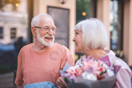 老年男和女走在街上和微笑交流的侧面图老太拿着一束鲜花他们幸图片