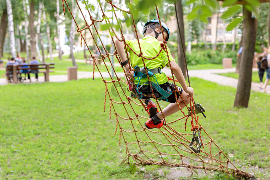 小男孩在冒险公园的绳子墙上爬安全设备图片