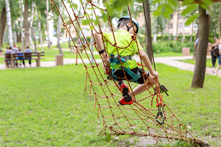 小男孩在冒险公园的绳子墙上爬安全设备图片