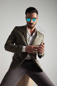 穿着太阳眼镜的感时尚男子坐在浅灰色背景的木盒子图片