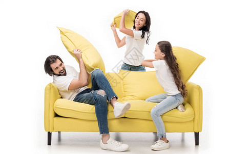 在黄色沙发上穿着白衬衫的幸福家庭枕头争斗在图片