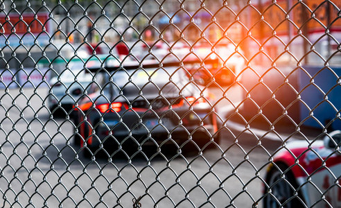 在柏油路上赛车从赛马场背景上模糊的汽车上的栅栏网看街道赛上的超级赛车图片