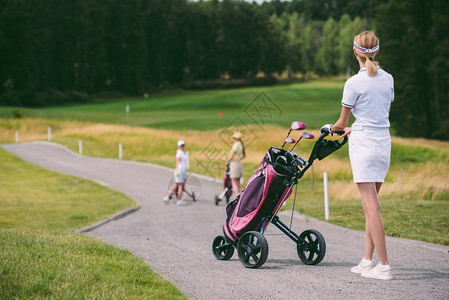 女高尔夫球手在高尔夫球场戴帽和带高尔夫装备的白色马球图片