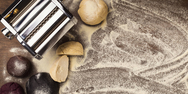 面食机和生面团在撒了面粉的厨房桌子上自制意大利宽面条的制备顶视图片