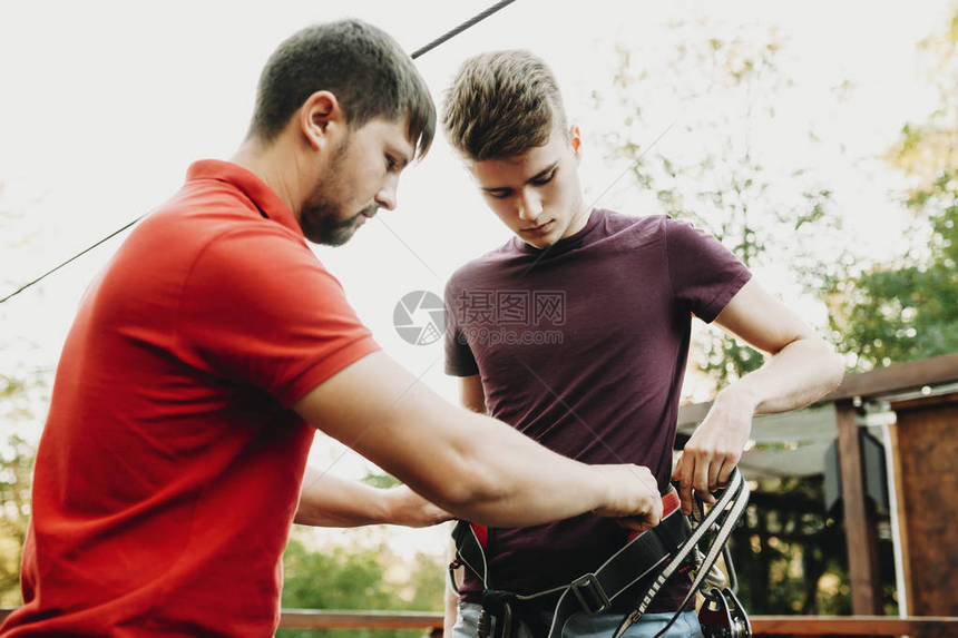 成年工作人员男子帮助身着安全套的青年男子站在夏月公图片