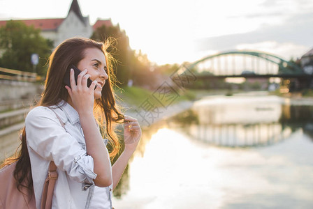年轻美丽的女孩晚上在日落时河边享受电话交谈图片