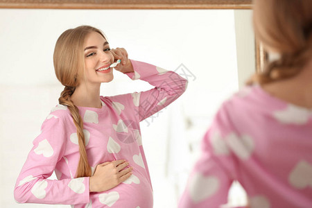 年轻孕妇在浴室清洁牙齿图片