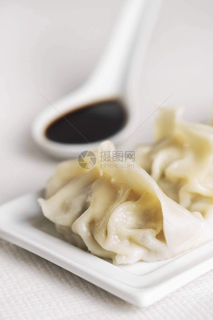 一些亚洲饺子或饺子在白色陶瓷盘和白色陶瓷勺形酱油碗上的特写图片