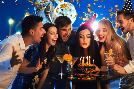 年轻女人在生日蛋糕上吹蜡烛和俱乐图片