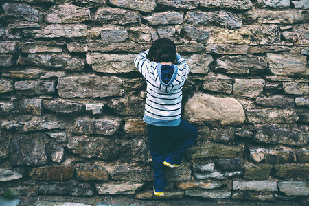 男孩爬上石栅栏孩子正试图爬上石墙一堵旧砖墙一个小的攀岩者图片