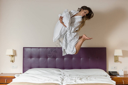 美丽的女人玩得开心在浴袍里跳上床枕头图片