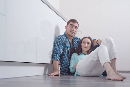 年轻夫妇坐在白色厨房内面的大厅地板上图片