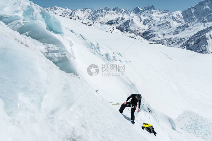 一位戴着头盔和滑雪面罩的专业登山者在冰川上切开冰斧冬季专业登山者在蓝天下的图片