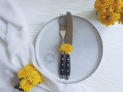 白色木制背景上的盘子叉子刀子菊花图片
