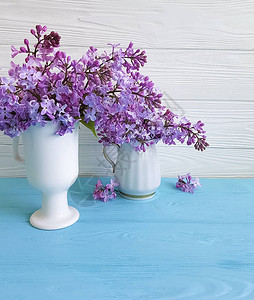 蓝色木质背景上丁香花的枝条花瓶图片