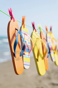 在沙滩上挂在一条衣服线上的两对多彩的翻滚拖鞋海洋背图片