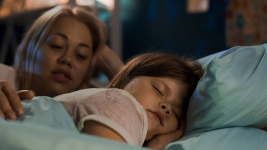 美丽的女人和可爱的小女孩躺在床上在睡着前讲童话图片