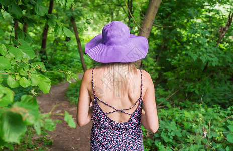 穿着紫罗兰帽子和紫罗兰裙子的女人穿过树图片