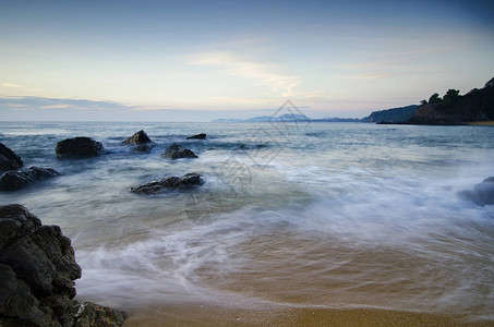 美丽的白色波浪流在黑暗云层背景的沙背景图片