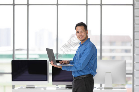 亚洲青年商人站在现代办公室以幸福的方式持有新的笔记本电脑图片