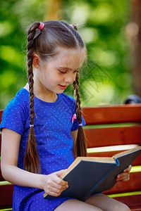 坐在木板凳上手握开放书籍的可爱柔软小女孩肖像图片