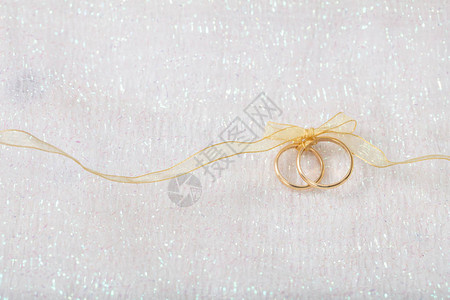 一对金婚戒指绑着金丝带在白闪亮的背景图片