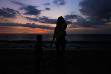 日落背景下与小女孩在海边散步的女剪影母亲和孩子图片
