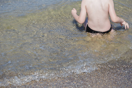 男孩背坐在海水中图片