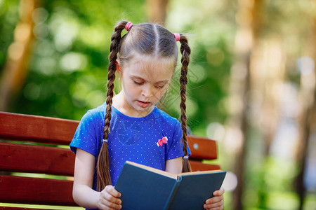 坐在木板凳上手握开放书籍的可爱柔软小女孩肖像图片