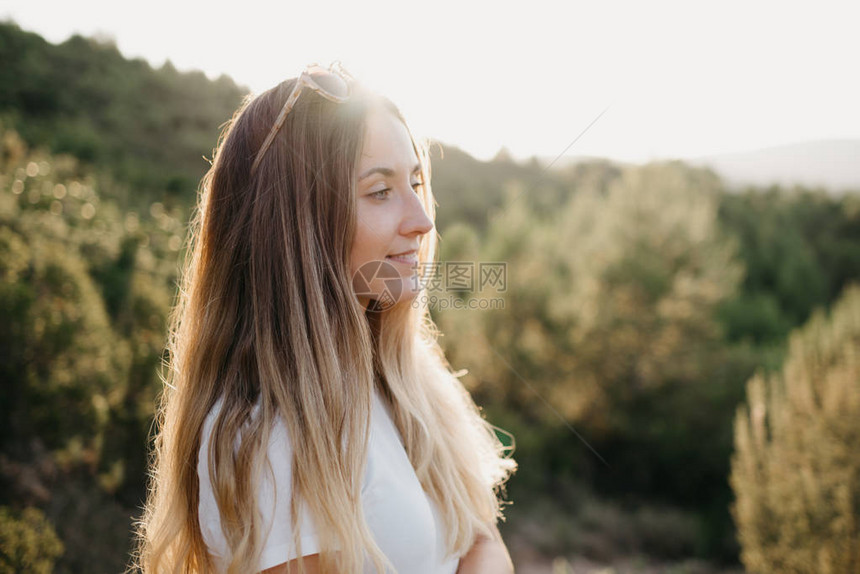 可爱的女孩在T恤和太阳镜摆在沙路上很多绿色植物与青山和日落在西班牙的背景图片