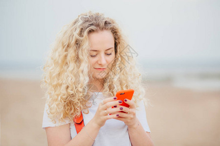 令人愉悦的卷发女户外肖像使用现代手机进行在线交流图片
