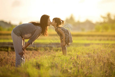 母亲与女儿亲吻和在田野玩乐的陶艺在美丽的日落中图片