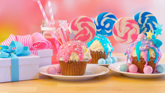 三个粉色和蓝色主题彩色新奇纸杯蛋糕装饰着糖果和大心形棒糖图片