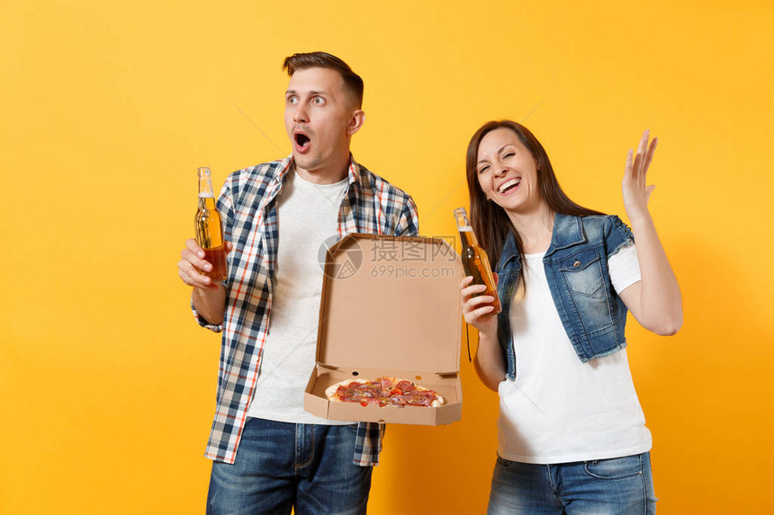 年轻惊讶的夫妇女人男体育迷们振作起来支持团队拿着啤酒瓶意大利比萨饼在纸板平箱传播手孤立在黄色背景运动家庭图片