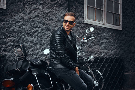身着黑色皮夹克和牛仔裤的时装年轻摩托车手穿着太阳镜图片