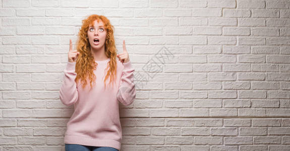站在砖墙上站着的年轻红发妇女惊讶地仰望起来图片